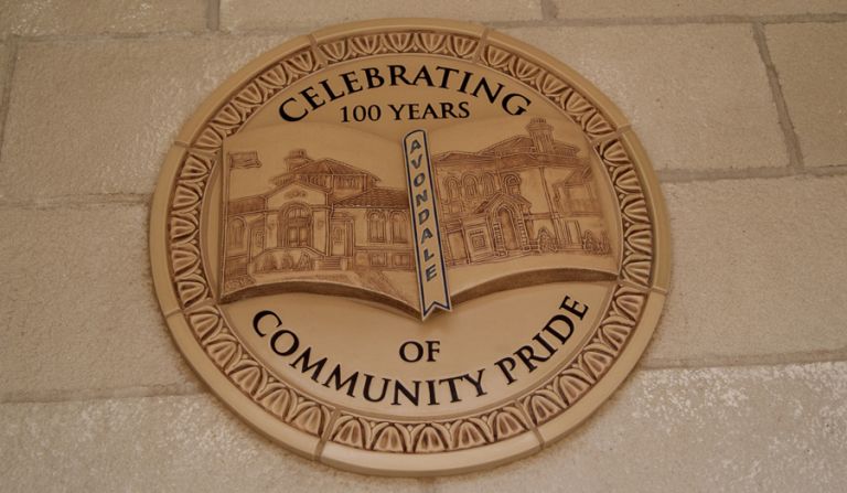 Circular Rookwood ceramic medallion mounted on a stone wall reading "Celebrating 100 Years of Community Pride" with an "Avondale" banner, depicting historic Avondale library buildings in relief